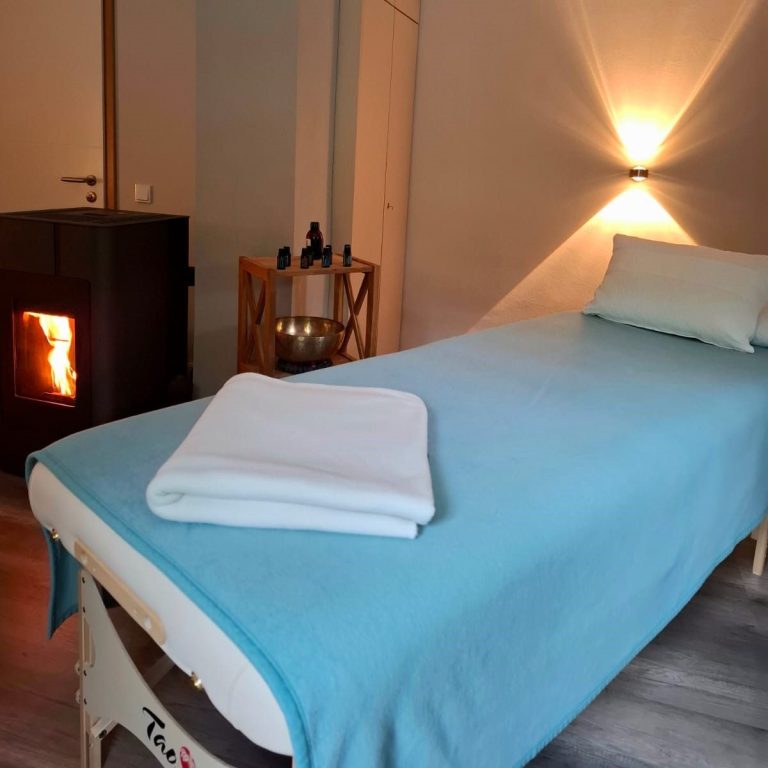 Meine Wohlfühloase Wohlfühlraum mit Massagetisch, Klangschalen und einem Kamin.