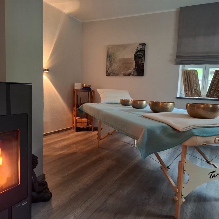 Mein Wohlfühloase Ruhiger Wellnessraum mit Massagetisch, Klangschalen und Kamin.